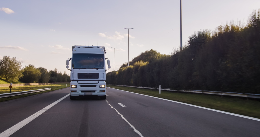 Cargo truck with cargo trailer driving on a highway. White Truck delivers goods in early hours of the Morning - very low angle drive thru close up shot. | Shutterstock HD Video #1058088760