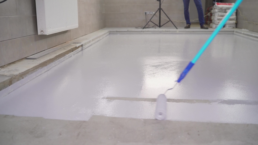 floor painting. dirty repairs and alterations. A worker paints the floor white with a roller. The concrete floor is painted with white paint. In focus Paint roller with defocused background. Royalty-Free Stock Footage #1058092519