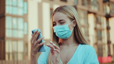 Close up blonde woman in protective medical mask stand on street uses phone news covid19 coronavirus virus protection pandemic city slow motion