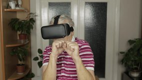 Senior grandfather in virtual headset glasses watching 3D video in VR helmet and training box, shows fist fight. Active healthy lifestyle sporty old man in VR goggles playing games, indoor exercising