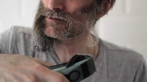 Middle-aged man cuts the remaining facial hair after shaving long half-gray beard Quarantine