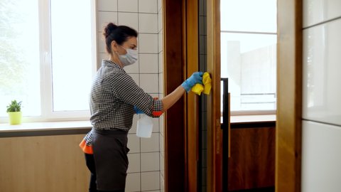 female cleaning lady, in protective mask and gloves, wipes door handles with antiseptic in restaurant or public establishment. protection against coronavirus, safety concept