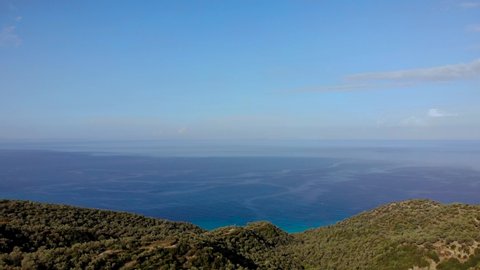 Endless sea horizon with blue aquamarine water bordering green hills with olive plantations in Albania