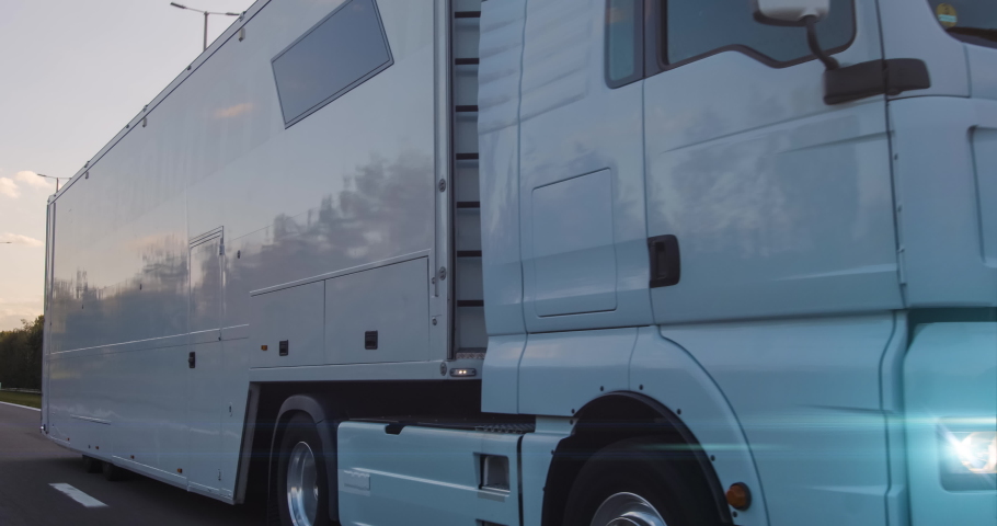 Cargo truck with cargo trailer driving on a highway. White Truck delivers goods in early hours of the Morning - very low angle drive thru close up shot. Royalty-Free Stock Footage #1058100298