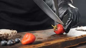 Slicing fresh strawberry on wooden cutting board. Skow motion food video. Restaurant concept. Close-up of chef in black gloves cutting strawberries on chopping Board in restaurant kitchen. Full hd