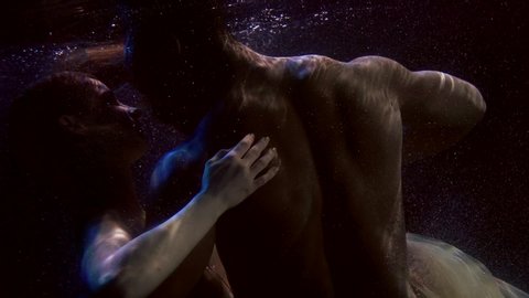 romantic loving pair is floating underwater in dark pool, lovers are caressing and kissing
