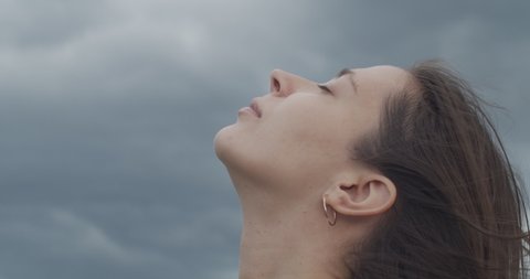 Close up portrait of female face looking up into stormy sky copy text space. Detailed macro side view of woman with closed eyes on nature rainy background slow motion. Facial care cosmetics products