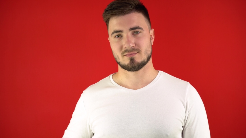 Attractive man on a red background winks his eye and drinks soda from a glass glass. Youth concept. Studio video, isolate, 4K.