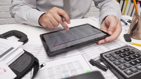 Business analysis and accounting concept - businessman working with document, spreadsheet, using calculator, tablet pc. Office desk closeup. 
