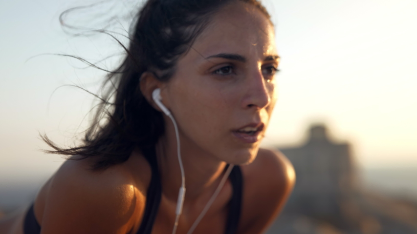 Close up of an young active sporty athlete smiling woman is taking a break after making running and jogging workout on a top of rock with seascape at sunset. Royalty-Free Stock Footage #1058114491