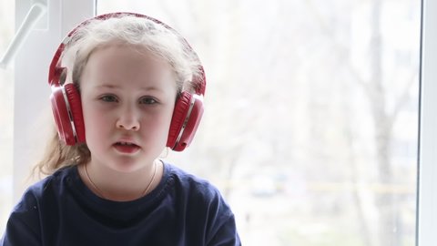 A little girl in red headphones sets up music playback for herself. The child listens to music through headphones. Happy childhood. Selective focus