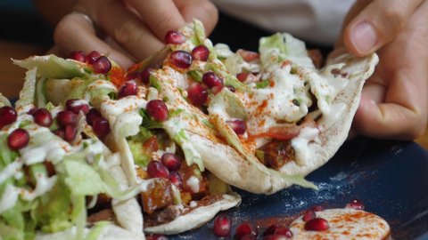 Close up of hands picking on of healthy vegan pita stuffed with veggies under vegan mayo sauce and pomegranate seeds. Healthy vegan lifestyle. 