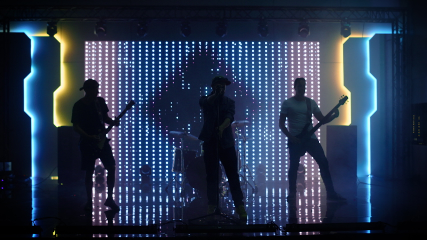 Four Man Rock Band with Lead Singer, Guitarists, Bassist and Drummer Performing at a Concert in a Night Club. Live Music Party in Front of Bright Colorful Strobing Lights on Stage. Royalty-Free Stock Footage #1058126545