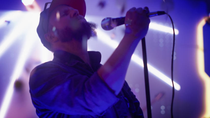Rock Band Performing at a Concert in a Night Club. Portrait of a Lead Singer Singing into Microphone. Live Music Party in Front of Bright Colorful Strobing Lights on Stage. Royalty-Free Stock Footage #1058126791