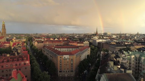 Rainbow over Stockholm city aerial view. Drone shot flying over buildings in central Stockholm, cityscape skyline at sunset, rainy sky