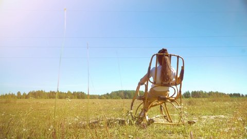 Alone beautiful Woman relaxing and sitting on rocking chair in the grass field. Lifestyle and travel concept