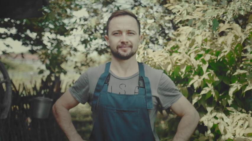 Worker in the garden. Young adult man stands in the summer garden and looks at the camera. Color graded