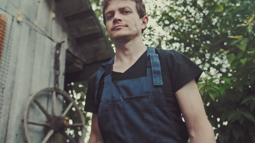 Worker in the garden. Young adult man stands in the summer garden with hammer and looks at the camera