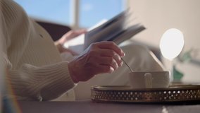 Relaxation time: A mature woman sits in an armchair reading a magazine and stirring sugar in a coffee mug. Only hands in the frame, no face. An adult woman drinks coffee in a sunny room. - Powered by Shutterstock - Get 15% off with code: PIKWIZARD15