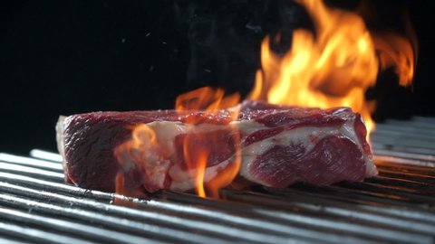 Cooking juicy meat steak in burning charcoals fire on bbq grid, flames and smoke.