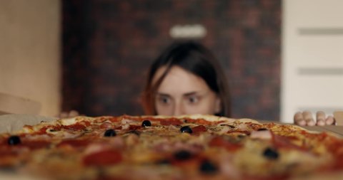 A young beautiful woman is tempted to eat a slice of pizza and breaks the diet. Close up of pretty young girl enjoying the smell of a pizza