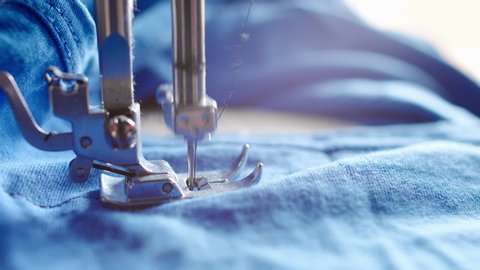 Fast movement of the sewing machine needle on the blue fabric. The needle of the sewing machine stitches the fabric. Close-up of the sewing machine needle
