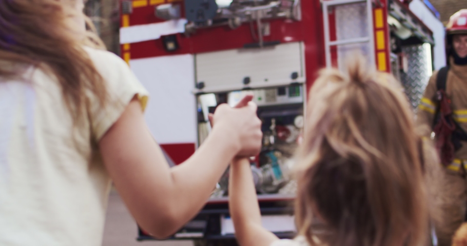 Middle plan injured little girls sisters reunites with their loving father fireman in helmet and gull equipment. In background fire truck. The concept of saving lives, heroic profession, fire safety Royalty-Free Stock Footage #1058149831