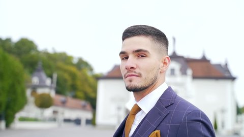 close-up portrait of a young attractive man with a beard in a suit and tie. looks away and into the camera. Stylish fashion groom on the outside. Fashion confident businessman standing alone. Wedding