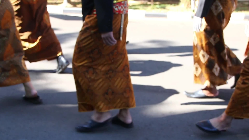 a group of people walking while wearing Javanese clothes, beskap and jarit, in the form of batik cloth.