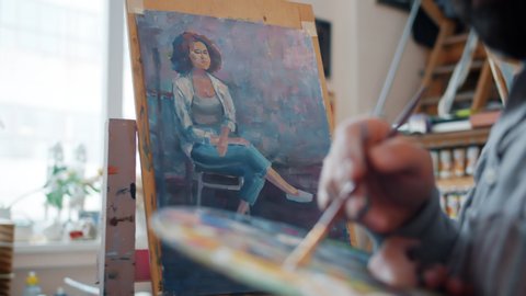 Slow motion of skilled artist painting portrait of young woman working in studio alone using paintbrush palette and paper on easel. Culture and hobby concept.