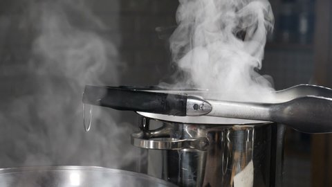 Steam or Vapour clouds coming from boiling water in saucepan on stove. Steam clouds from pan while cooking. Cooking process in slow motion. Steam and white smoke rising on dark background. Full hd