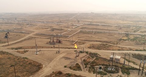 Gas flare coming out of a flare stack in California, vast oil fields with pipelines transporting oil from oil pumps, aerial drone shot