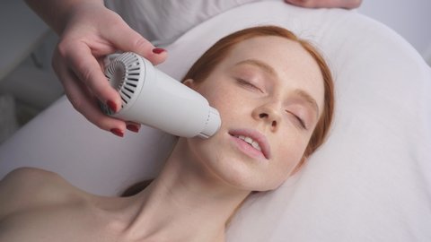Beautiful woman at a cosmetologist's reception receives a vacuum massage of the skin of the face using a cosmetological device.