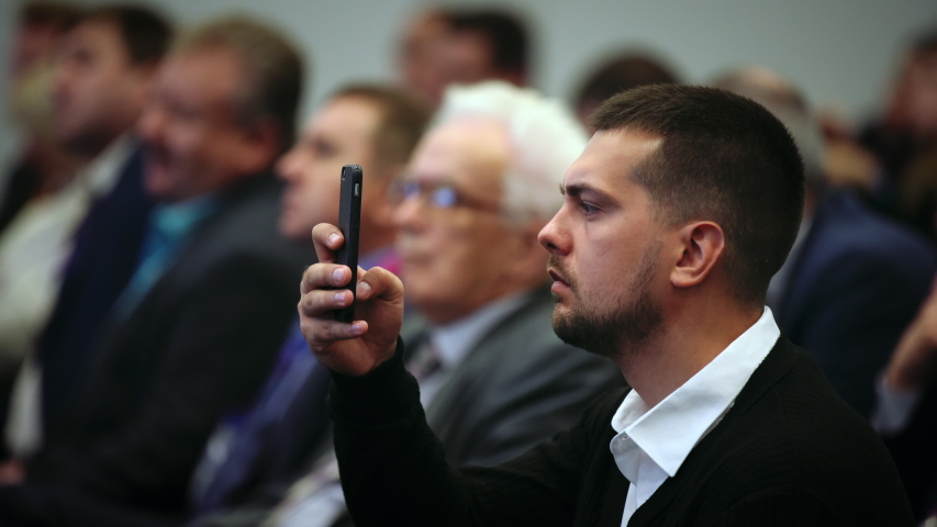 Person take photo on phone in crowded audience business forum. Conference business man with mobile. Seminar for viewer auditorium. group people listen speaker speech. Taking photography scene on phone