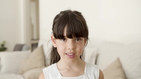Happy pretty black haired girl standing in living room, looking at camera, smiling and posing. Closeup shot, front view. Child at home or male portrait concept