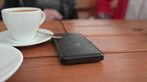 The girl in the cafe connects the phone to the power bank for charging and puts it on the table.