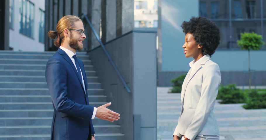 Caucasian young businessman and African American businesswoman shaking hands outdoors when meeting. Business mixed-races male and female partners at city street. Multi ethnic man and woman making deal Royalty-Free Stock Footage #1058170255