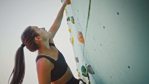 Close up shot of young woman climber going up on an outdoor rocky wall.