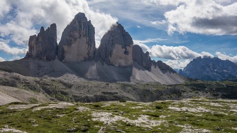 Time lapse of the clouds moving over the Three Peaks of Lavaredo in the Dolomites with blue sky and green grass on the foreground