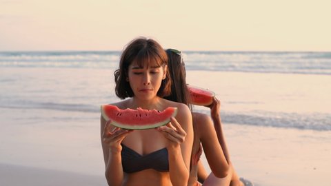 Travel concept. Asian young woman sitting by the beach eating watermelon. 4k Resolution.