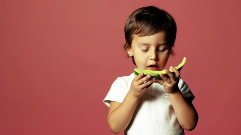 Happy child eating watermelon. The child is eating fruit in the studio. Little girl biting a slice of watermelon and show like with hand