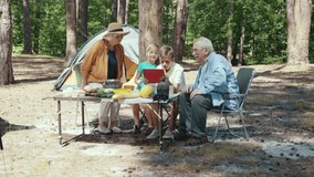 Kids and grandparents enjoying summer holiday weekend picnic. Adorable family using tablet computer communicating with parents from the forest nature.