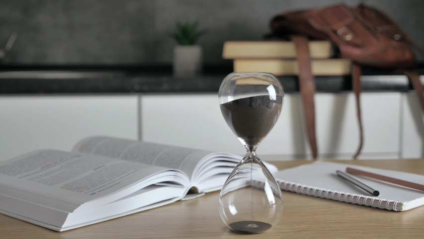 Pouring sand in an hourglass standing on the desk in workspace. Distance education concept. Working desk: books, pen, backpack and other tools 4k Royalty-Free Stock Footage #1058193586