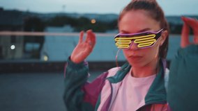 Fashion woman with sunglasses and earrings dancing outside looking at camera. Outdoor portrait. Female dancer performing dance show making freestyle stunts. Funny stylish caucasian hipster girl. 4K