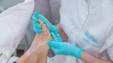 Skilled professional massaging the feet of the client with a lotion under sterile conditions during pedicure session. Close up.