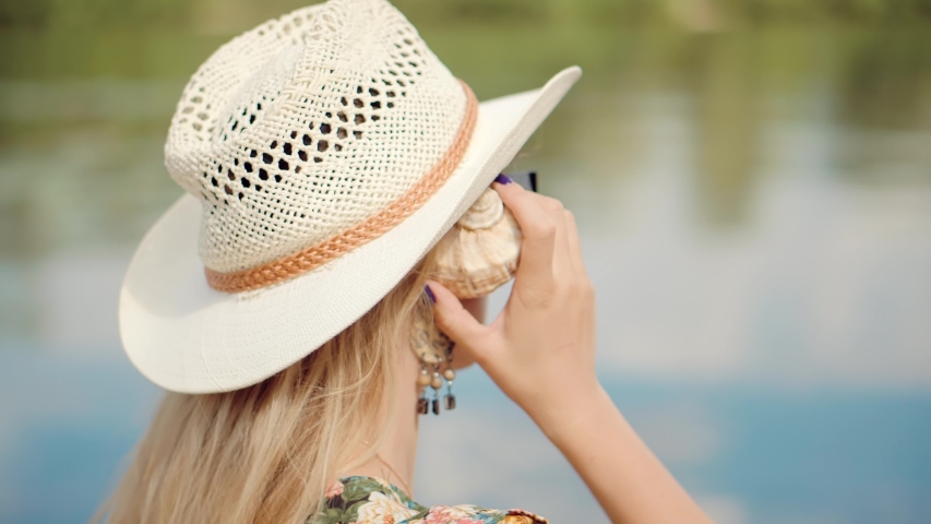 Dreaming Woman Relaxing Trip On Summer Days.Woman Holding Sea Shell In Hand And Listening Noise.Pretty Girl In Hat Having Fun On Holiday Vacation Weekend.Lady Listening Sound From Sea Shell Up To Ear.