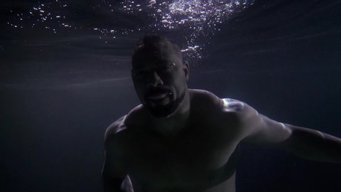 A middle-aged, attractive man is swimming underwater in the sea. Male model on the beach. Around the dark background and bubbles. Slow-motion underwater photography.