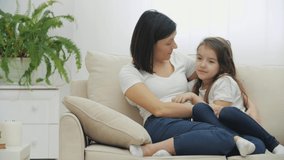 4k video of mother and her daughter talking and sharing secrets sitting on sofa at home.