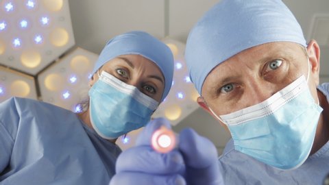 Doctor surgeon with assistant checks the reaction of the pupils of the eyes with bright light. The patient wakes up after a coma. First-person view
