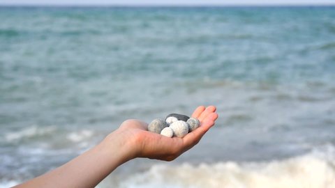 Blurry defocus Beautiful round gray and white sea stones lie in a female hand against background of sea and waves. The concept of relaxation, vacation and meditation, zen, Cyprus. Slow motion video.
